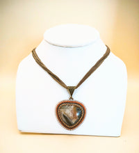 Load image into Gallery viewer, Necklace with a heart-shaped pendant on a white stand against a beige background